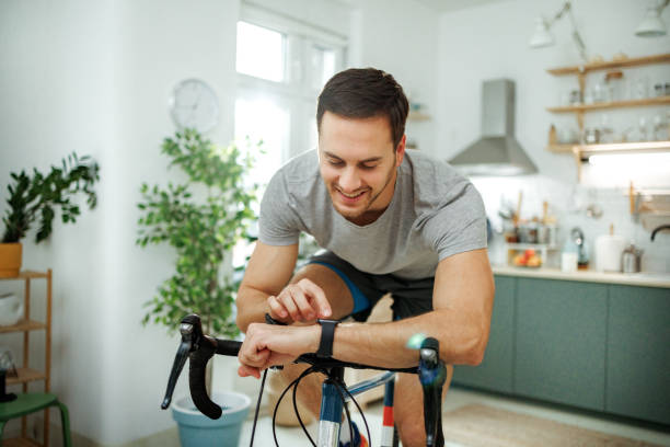 Man cycling on stationary bike, checking fitness watch in modern home setting, showcasing home workout essentials.