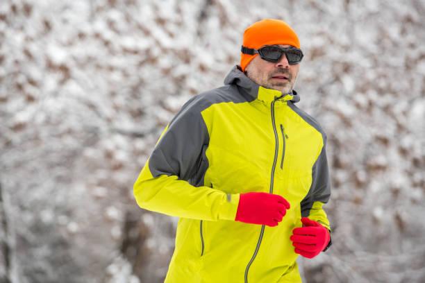 Man running in winter gear, including a green jacket, red gloves, and an orange hat, in a snowy environment.